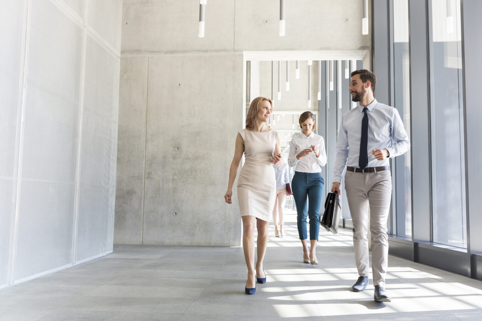 A group of businesspeople talking while walking through a bright hallway.