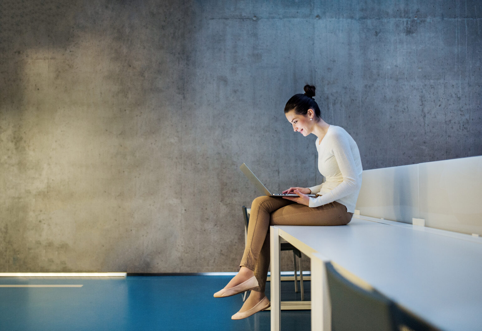 Seated woman on a computer with concrete wall in the background.