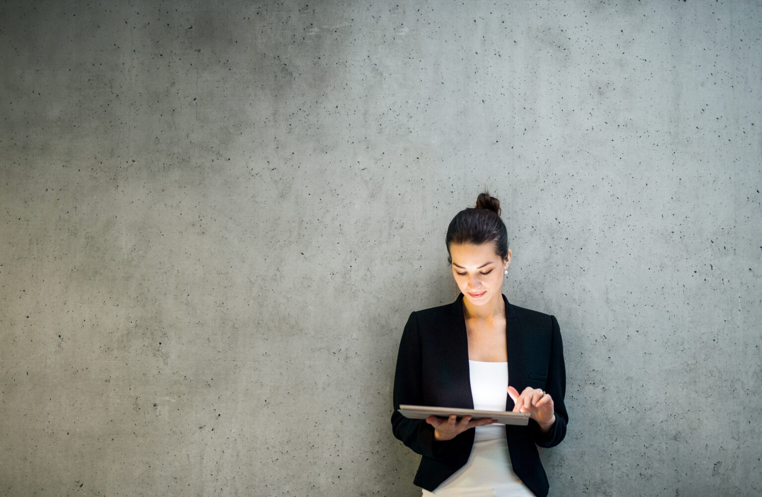 Young businesswoman leaning against a concrete wall working on a tablet computer.