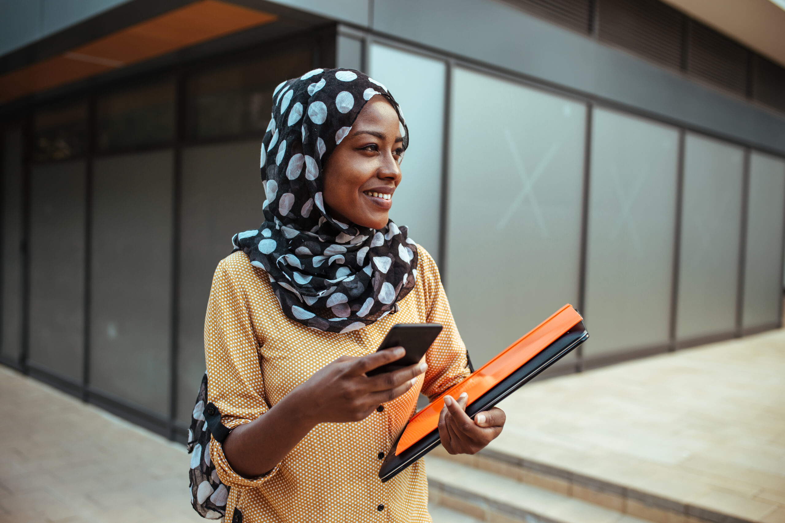 Smiling woman with head scarf dialing a mobile phone.