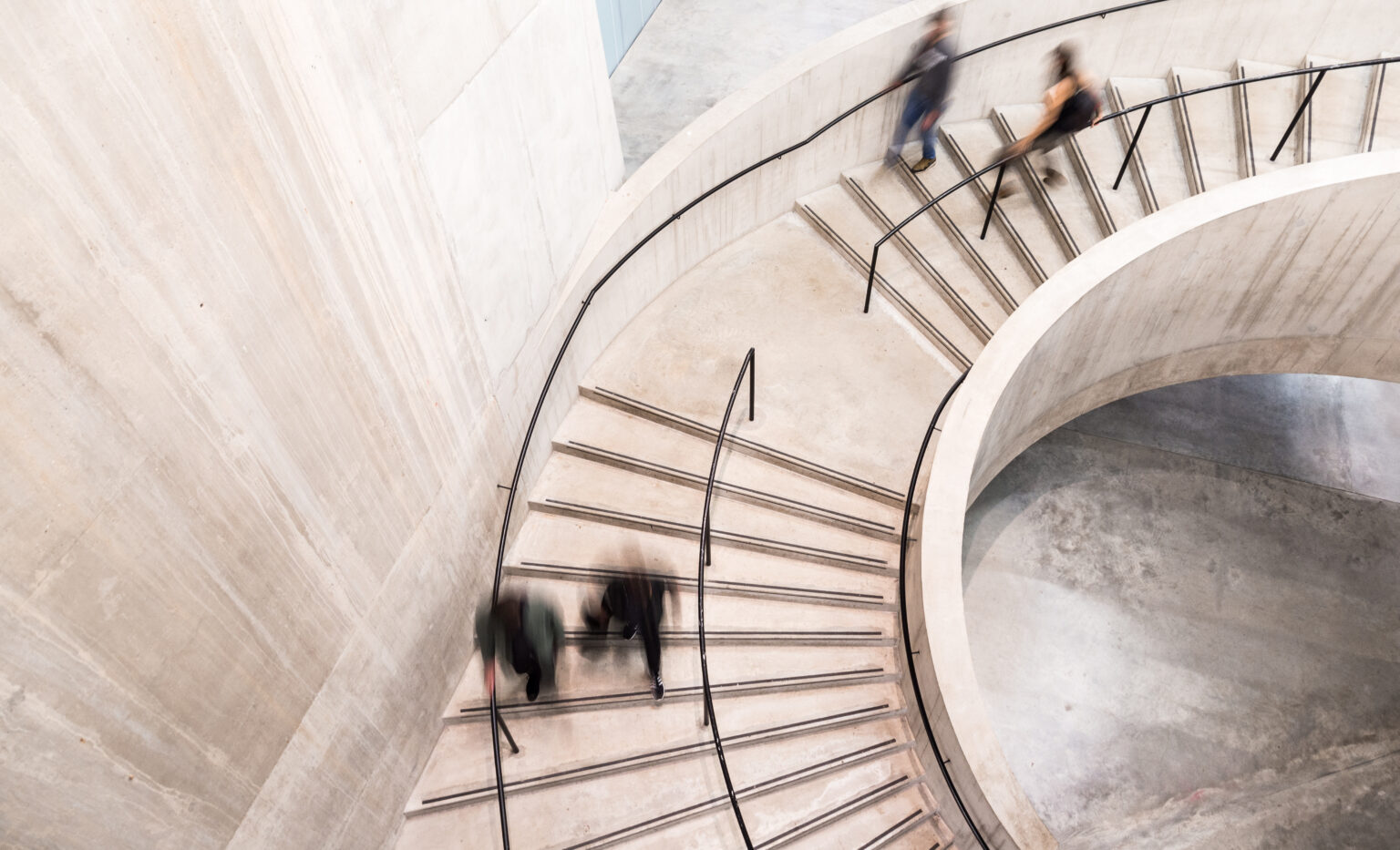 Motion-blurred businesspeople ascending a curved concrete staircase.