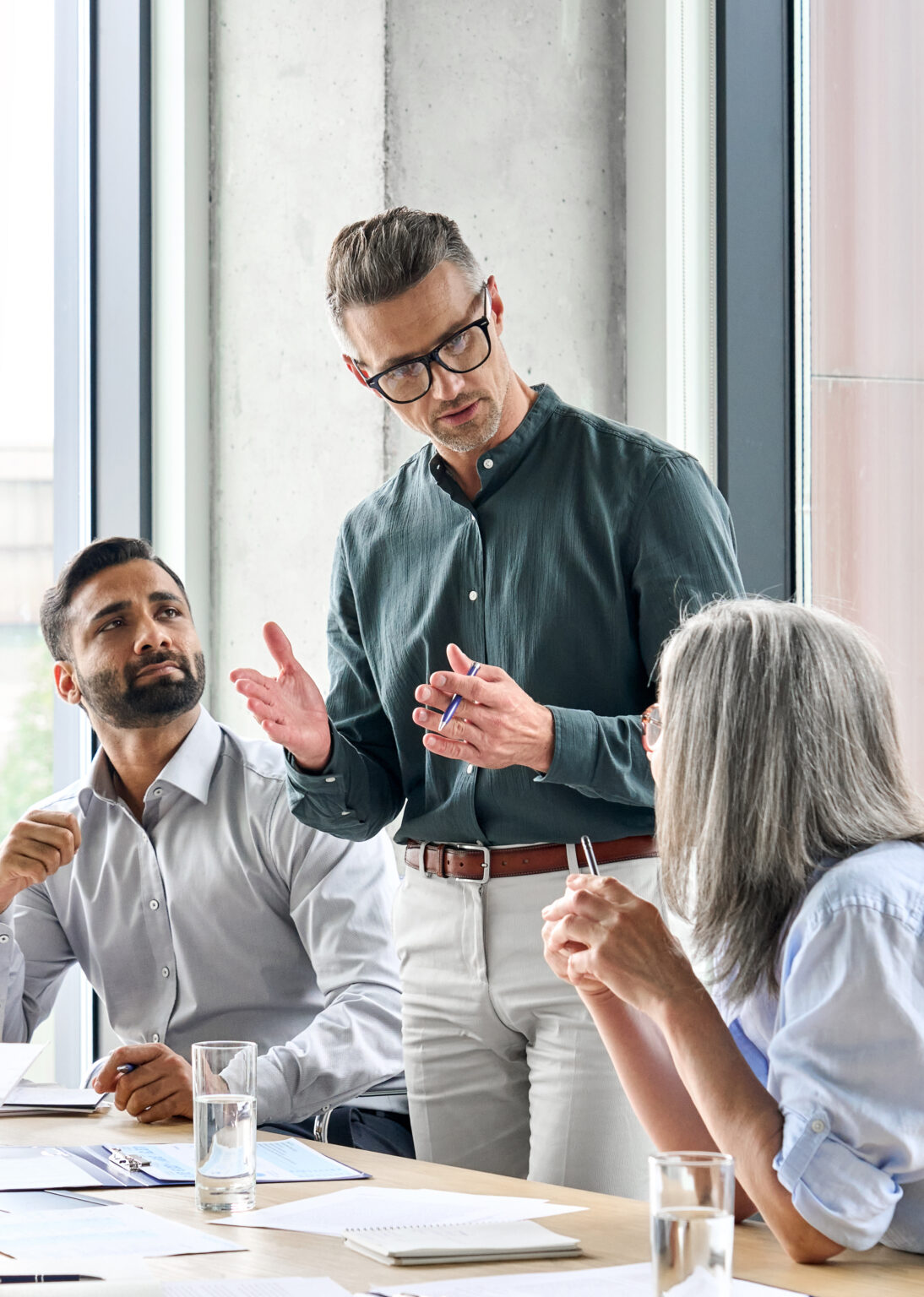 A small group of businesspeople in a meeting. One man is standing while talking to a seated woman.