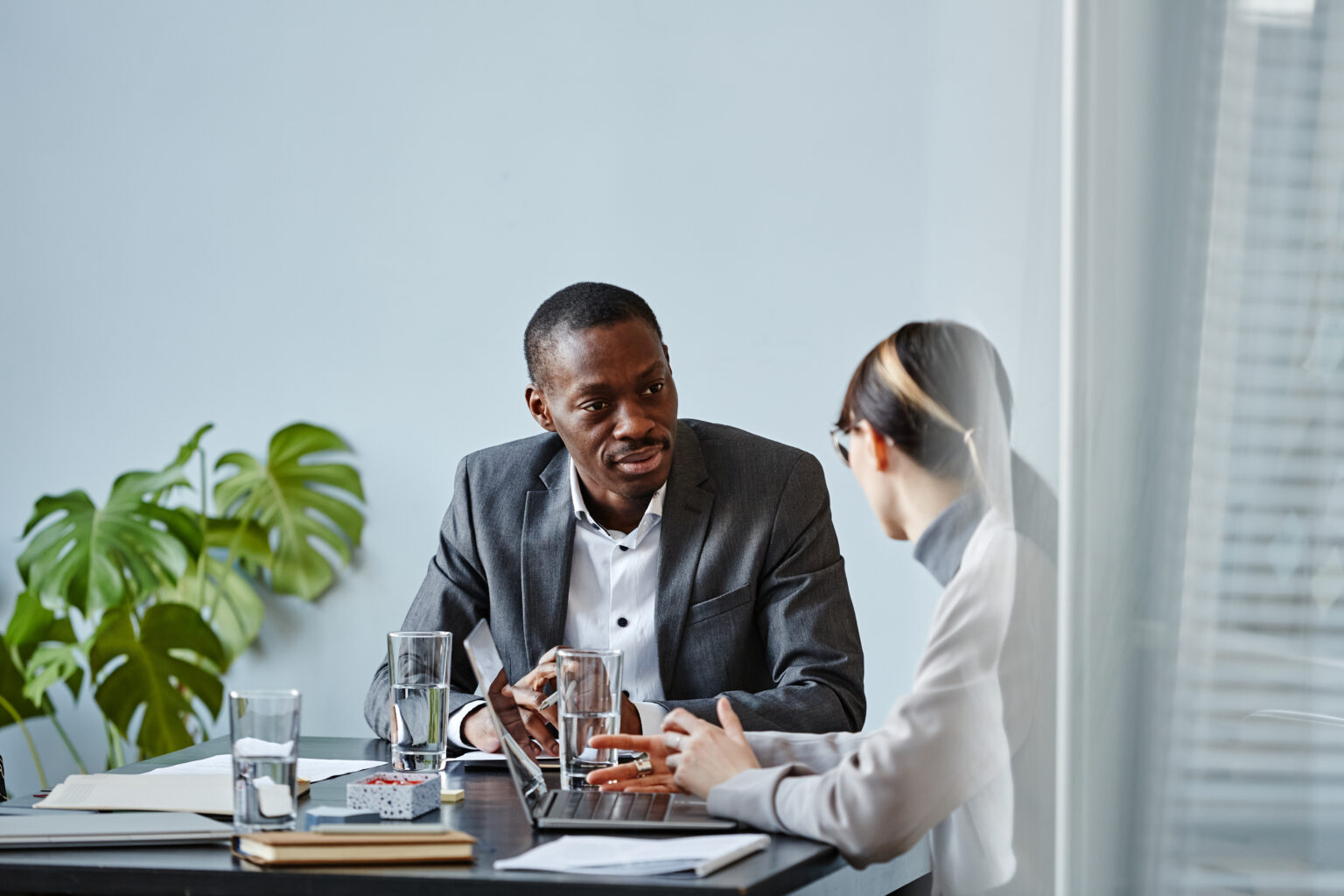 A businessman and businesswoman at a desk talking.