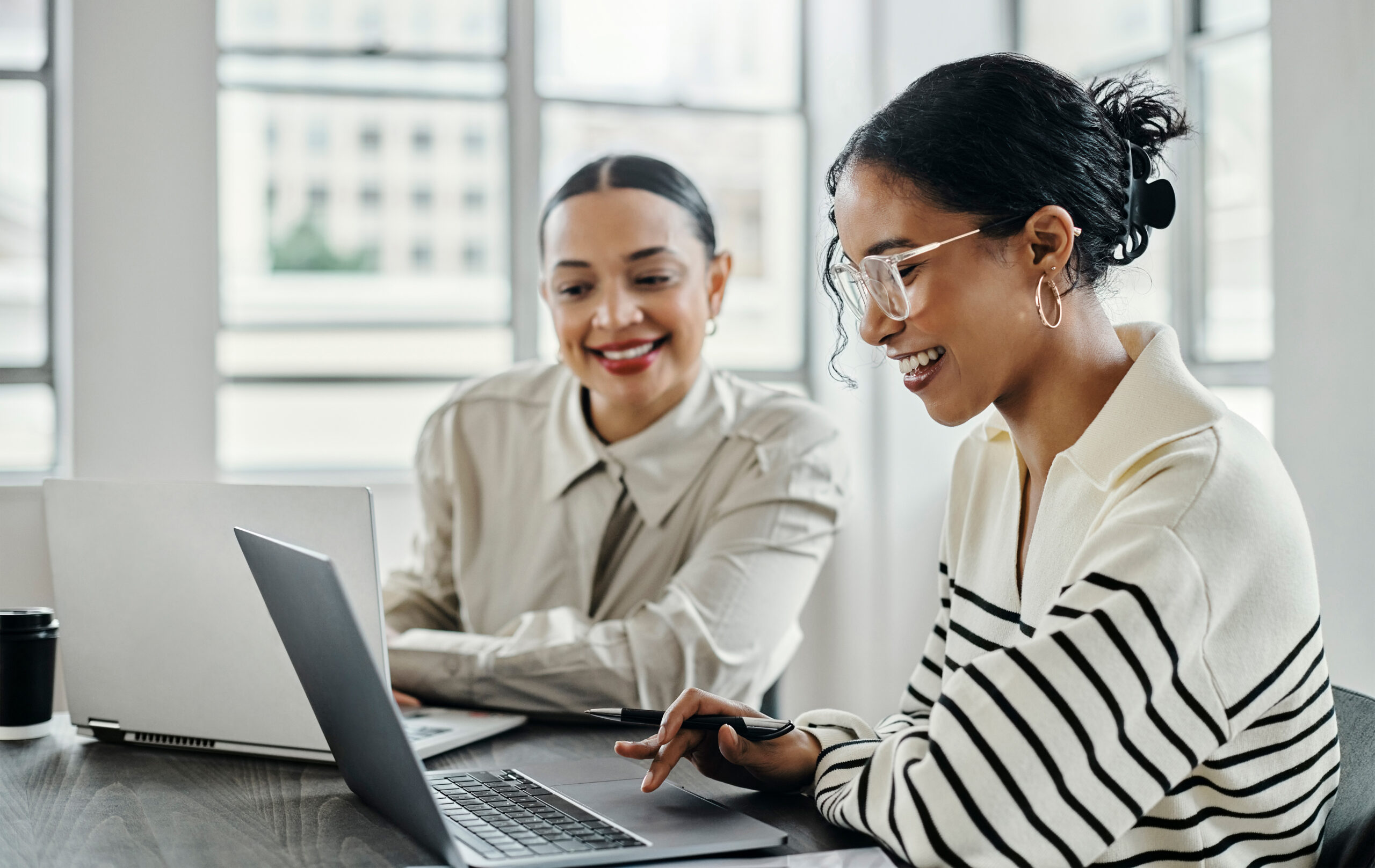 Two smiling businesswomen working on laptop computers together.