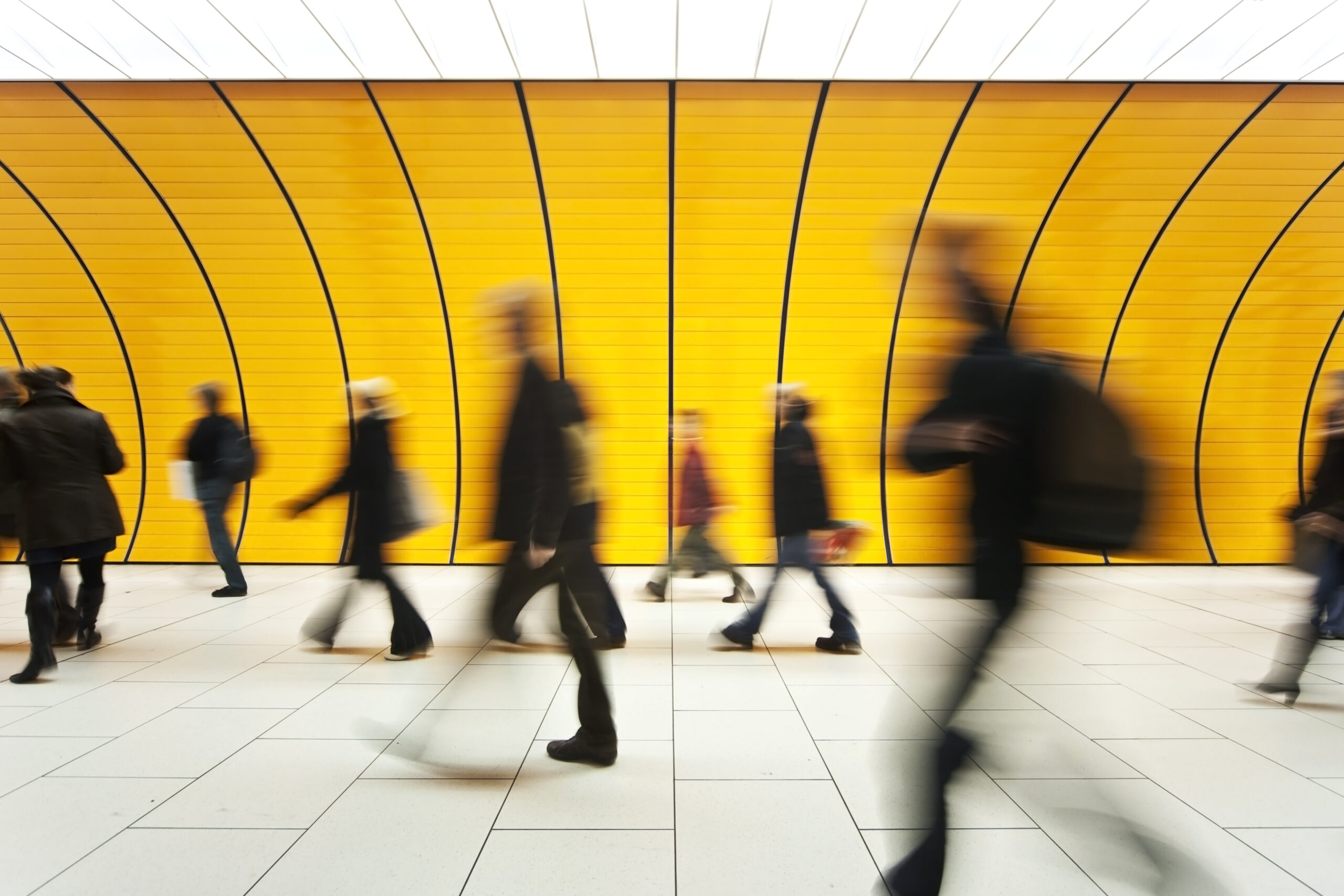 Motion-blurred shot of businesspeople walking through bright yellow hallway.