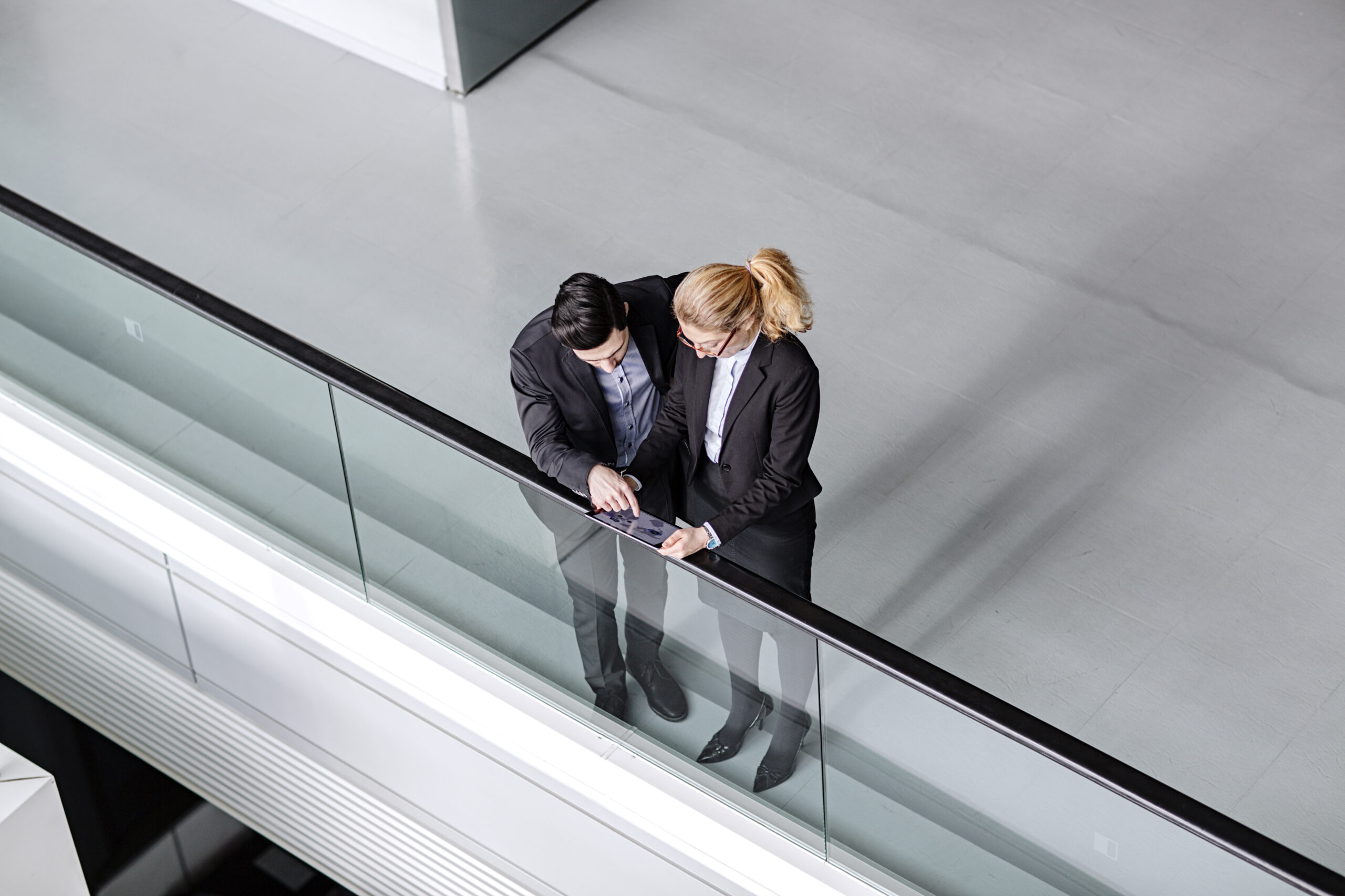 Businessman and businesswoman standing at the railing of an atrium having a discussion.