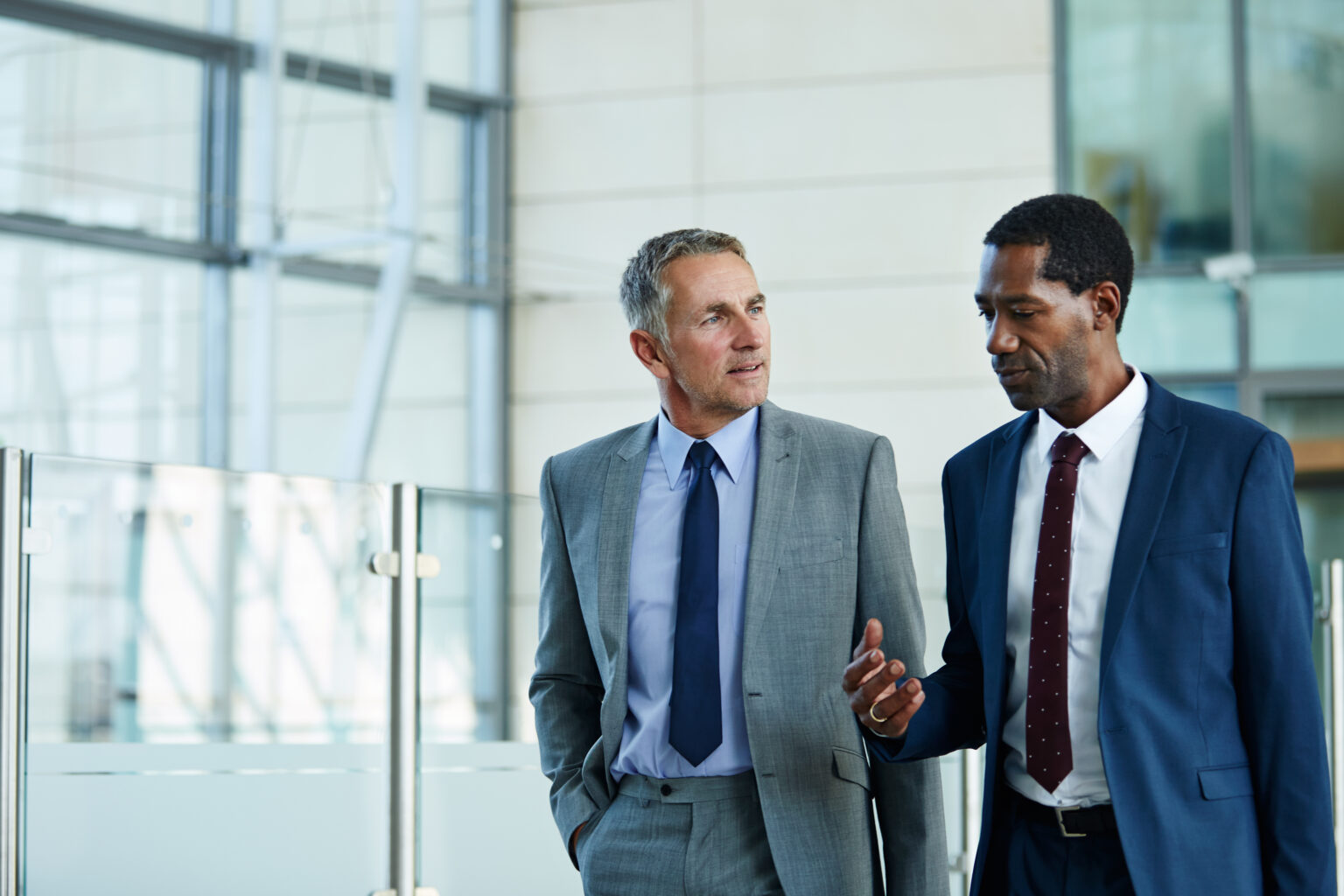 Two businessmen talking while walking through an office lobby.