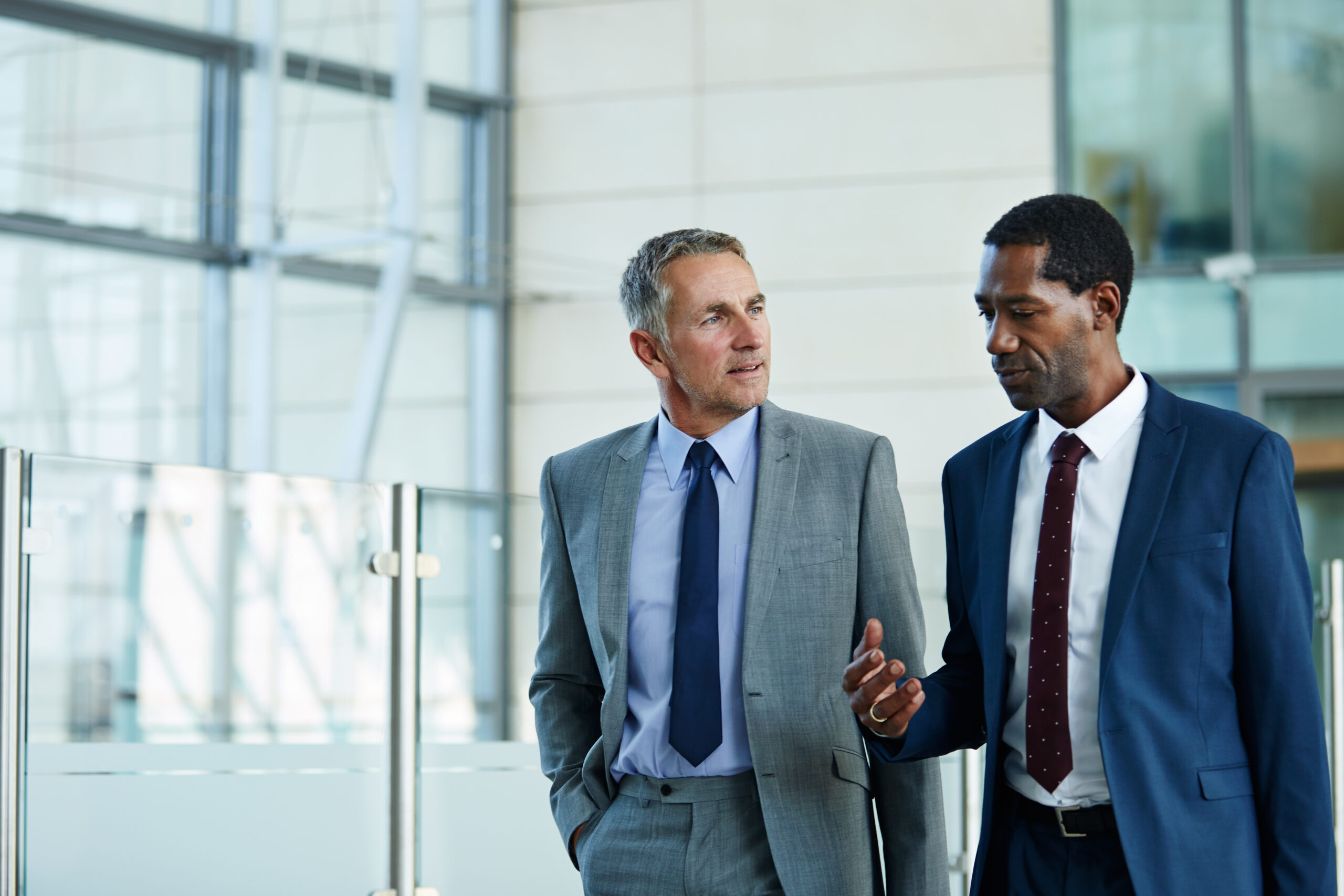 Two businessmen talking while walking through an office lobby.