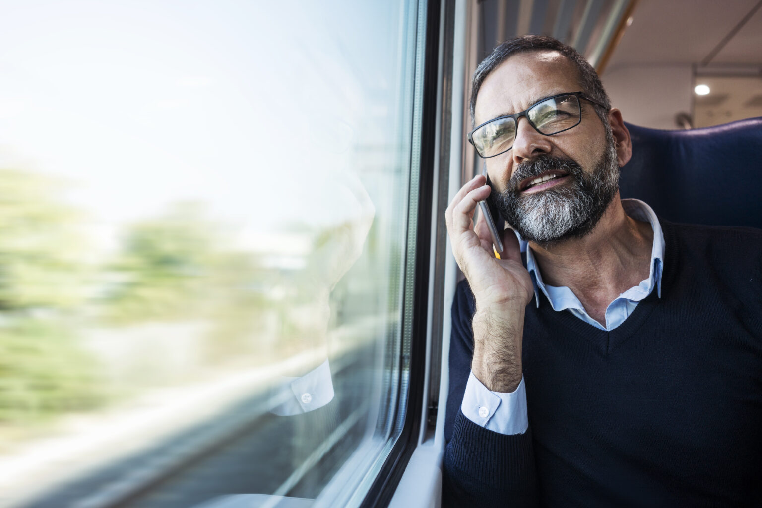 Man on train looking out of window while talking on a mobile phone.
