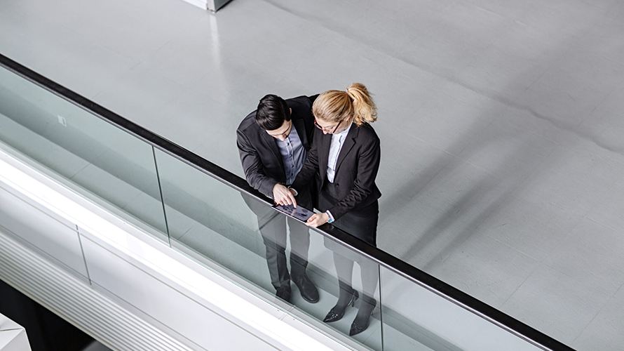 Businessman and businesswoman standing at the railing of an atrium having a discussion.